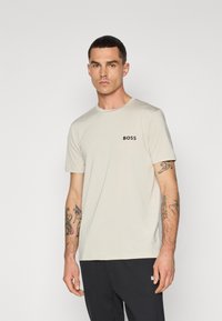 Beige, rövid ujjú póló, kerek nyakkal, bal mellen egy kicsi fekete "BOSS" logóval. Az anyag sima megjelenésű, könnyű textúrával.