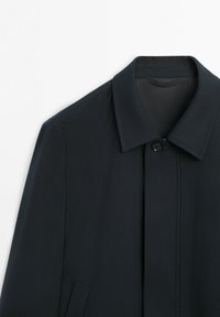 Czarny płaszcz na guziki z ostrym kołnierzem i boczną kieszenią, prezentowany na białym tle.