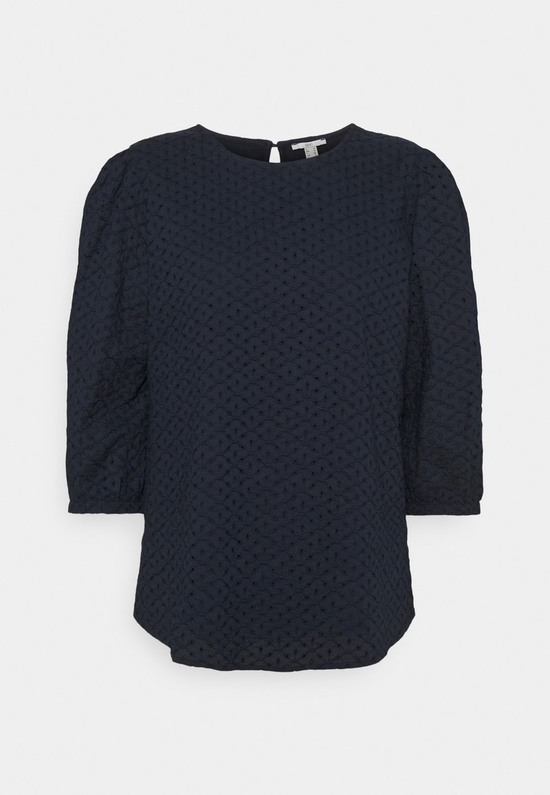 Blouse bleu marine avec manches bouffantes trois-quarts, tissu texturé présentant un motif en losange, encolure ronde et détail dos avec ouverture en forme de goutte.