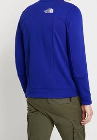 Královská modrá mikina s kulatým výstřihem a dlouhými rukávy. Na horní části zad je logo a steh detailů.