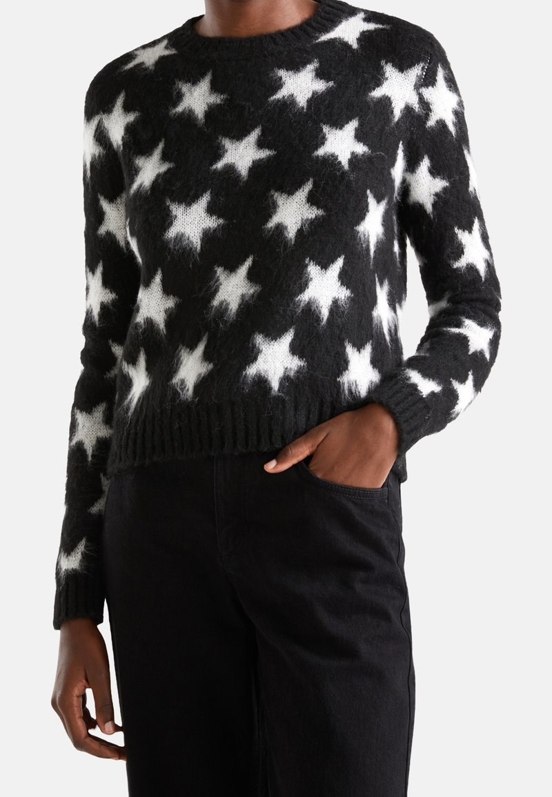 Svart stickad tröja med vita stjärnmönster, ribbad halsringning och nederkant, med långa ärmar och en mjuk, lurvig textur.