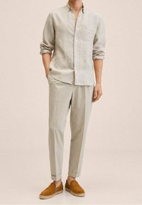 Chemise en lin boutonnée de couleur gris clair avec une poche poitrine unique, associée à un pantalon fuselé gris clair et des mocassins en suède marron.