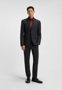 Completo da uomo grigio scuro con vestibilità slim, giacca a un petto, camicia bordeaux e cravatta coordinata. Scarpe eleganti nere completano l'outfit.