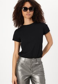 Black cotton t-shirt with rolled sleeves paired with shiny silver metallic pants. Model wearing oversized black sunglasses.