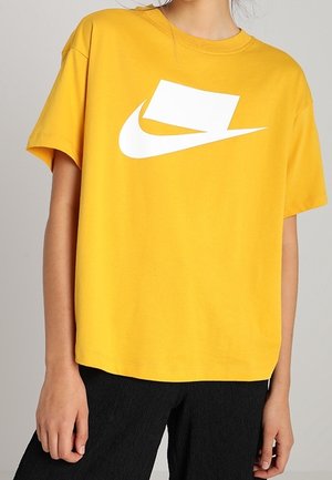 Žluté bavlněné tričko s velkým bílým logem Nike, s krátkým rukávem a volným střihem. Měkká textura s kulatým výstřihem.