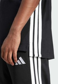 Sort atletisk tøj med hvide tre-stribede accenter på siderne og logo. Stoffet ser ud til at være struktureret og holdbart.