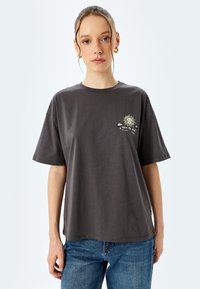 Grijze katoenen t-shirt met een frontgrafiek van een zon en de tekst "open the mind." Korte mouwen met een losse pasvorm.