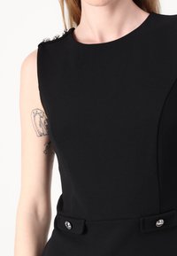 Rochie neagră structurat, cu decolteu rotund, trei butoane decorative pe o umăr și două accente cu butoane la talie. Textură netedă.