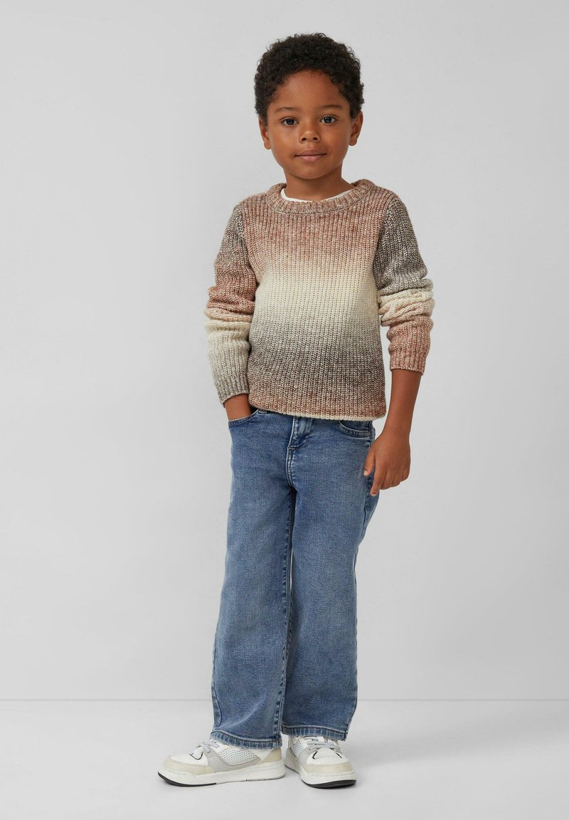Sweter z dzianiny w odcieniach ombre od brązu do beżu, w połączeniu z niebieskimi dżinsami i białymi trampkami. Casualowy, teksturowany design.
