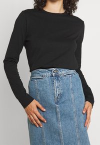 Svart långärmad skjorta i kombination med en ljusblå denimkjol med söm i fram, framfickor och knäppning.