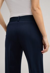 Dunkelblaue Hose mit glatter Textur und breitem Bund, der das prägierte "JOOP"-Logo trägt. Die Hose hat eine taillierte Passform und gerade Beine.