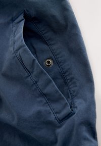 Gros plan sur un vêtement en tissu bleu marine avec une poche à rabat dotée d'une fermeture à bouton-pression noir.