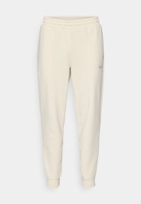 Pantalons de survêtement beige clair à cordon de serrage, avec une taille élastique, des chevilles resserrées, des poches latérales et un petit logo sur la cuisse gauche.