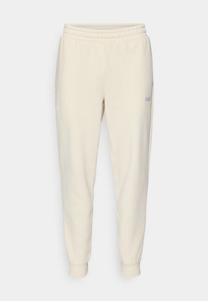 Pantalons de survêtement beige clair à cordon de serrage, avec une taille élastique, des chevilles resserrées, des poches latérales et un petit logo sur la cuisse gauche.