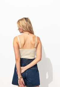 Débardeur beige à côtes avec bretelles réglables, associé à un short en denim bleu taille haute, vu de dos.