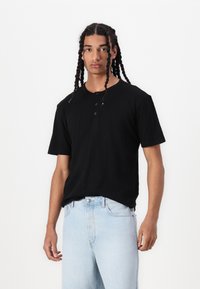 Black cotton short-sleeve t-shirt with three-button placket, relaxed fit, paired with light blue denim jeans. Smooth texture, simple design.