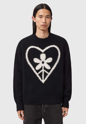 Svart strikkegenser med et hvitt hjerte- og blomsterdesign. Har rund hals og ribbestrikkede mansjetter og kant. Myk, strukturert stoff.