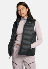 Gilet imbottito nero con zip frontale, colletto alto e isolamento leggero. Indossato sopra una maglietta a maniche lunghe rosa chiaro; presenta tasche laterali.