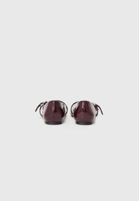 Ballerines en cuir verni bordeaux avec un profil bas, un bout arrondi et un détail de lien à l'arrière. Texture lisse et design minimaliste. Semelles noires.