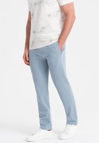 Hellblaue Hosen aus weichem Stoff, mit seitlichen Taschen und lockerer Passform, kombiniert mit einem weiß gepunkteten T-Shirt und weißen Sneakers.