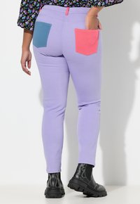 Wąskie dżinsy w kolorze lawendy z kontrastującymi tylnymi kieszeniami w odcieniach teal i koralowym. Gładka faktura z przeszyciami, zestawione z czarnymi masywnymi botkami.