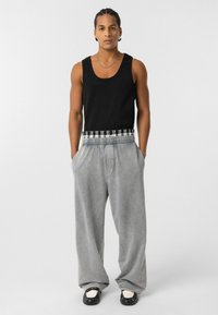 Zwart mouwloos tanktop gecombineerd met grijze joggingbroek met een gestreepte elastische tailleband; relaxte pasvorm met zakken. Getextureerde stof.