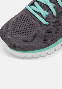 Chaussure de sport grise avec lacets turquoise et bordure de semelle, dotée d'une tige en mesh respirant et d'une semelle extérieure blanche texturée en caoutchouc.