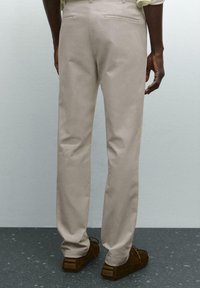 Beige trousers with a smooth texture, featuring a straight leg design and two back pockets, paired with brown slip-on shoes.