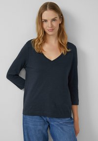 Navy-V-Ausschnitt Langarmoberteil aus weichem Stoff. Hat einen lässigen Schnitt und ein einfaches Design, kombiniert mit blauen Jeans.