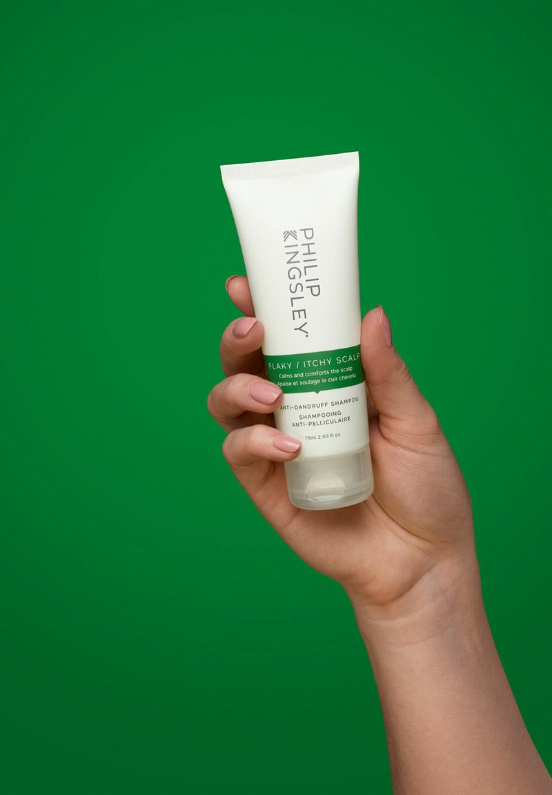 Phillip Kingsley Anti-Schuppen-Shampoo in einer quetschbaren weißen Tube mit grünen Akzenten, gehalten von einer Hand, vor einem grünen Hintergrund.