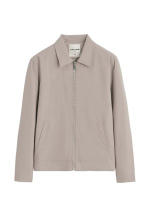 Veste décontractée beige clair avec fermeture éclair devant, deux poches en biais et un col pointu, étiquette indiquant la marque "Frilivin."