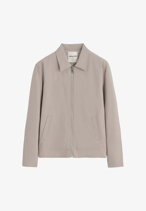 Veste décontractée beige clair avec fermeture éclair devant, deux poches en biais et un col pointu, étiquette indiquant la marque "Frilivin."