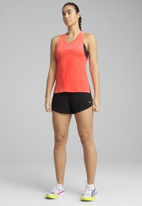 Top sin mangas de color coral con un diseño ajustado y aberturas laterales, combinado con pantalones cortos negros. Zapatillas con acentos en púrpura y amarillo.