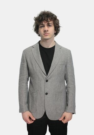 Blazer a righe in tessuto grigio e bianco, con un solo bottone, revers classici e tasche frontali. Indossato sopra una camicia nera.