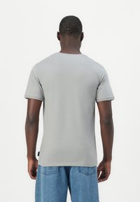Gray short-sleeve t-shirt with a round neckline, smooth texture, and a label on the left side, paired with blue denim jeans.