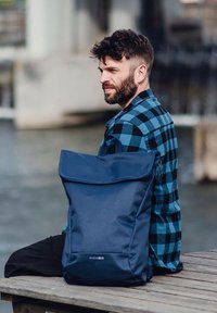 Marineblauem Rucksack mit gefaltetem Oberteil, aus strapazierfähigem Stoff. Rechteckige Form, minimale Hardware, mit glatter Textur und dezentem Logo.