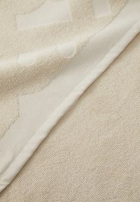 Asciugamano beige testurizzato con una superficie morbida, caratterizzato da un sottile motivo geometrico e un bordo liscio. Materiale morbido e assorbente.