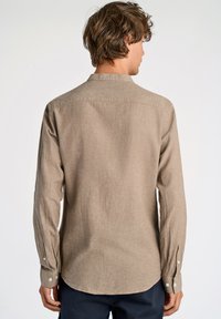 Camisa abotonada de color marrón claro con mangas largas, hecha de tela texturizada. Presenta un cuello clásico y puños abotonados; vista posterior mostrada.