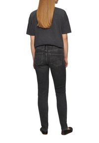 Czarna bawełniana koszulka i ciemne obcisłe dżinsy widziane z tyłu. Koszulka ma luźny krój, a dżinsy posiadają tylne kieszenie i elegancki design.