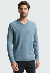 Helles blaues V-Ausschnitt-Pullover aus einem weichen, strukturierten Stoff. Lange Ärmel und gerippte Bündchen. Dezentes Logo-Detail auf der Brust.