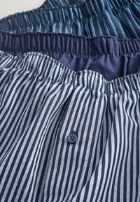 Drei Paar Shorts mit elastischem Bund in Marineblau und hellblauen Streifen. Zu den Merkmalen gehören geraffte Taillenbänder und ein Knopfdetail bei einem Paar.