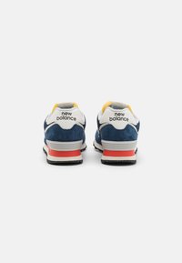 Navy blue sneakers with suede upper, white accents, yellow lining, and a red heel counter. Features New Balance logo on the back.