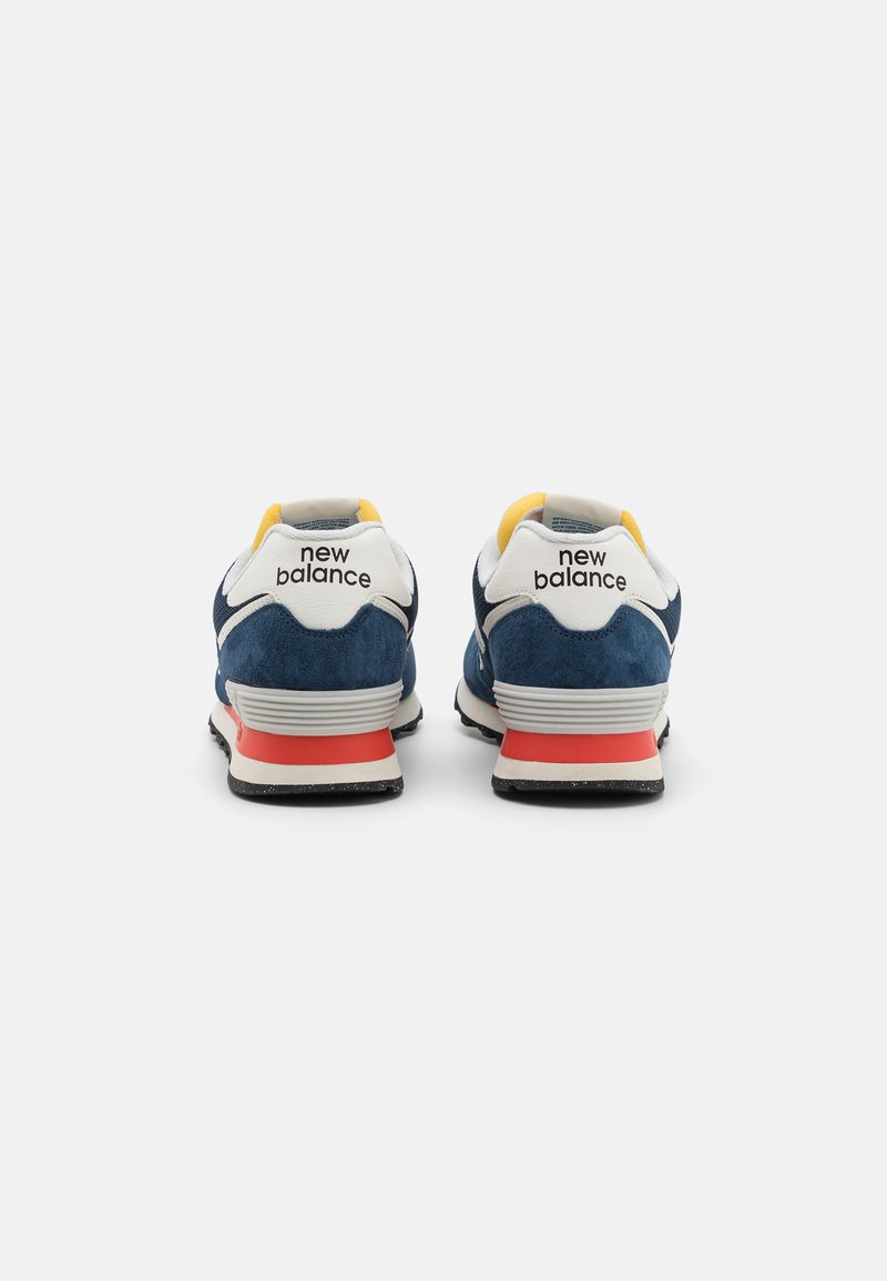 Baskets bleu marine avec dessus en daim, accents blancs, doublure jaune et contrefort rouge. Logo New Balance à l'arrière.