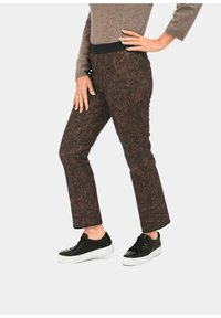 Bruine broek met een patroon en een zwarte tailleband, gecombineerd met zwarte sneakers. De stof heeft een bladdesign en een aansluitende pasvorm.