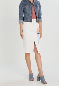 Denimjakke, pink top, hvid blyantskørt med blomsterbroderi, sideslids og blå åbne sko. Moderne afslappet outfit.