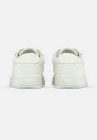 Λευκά αθλητικά παπούτσια με λεία δερμάτινη επιφάνεια, στρογγυλή μορφή, �επενδυμένα κολάρα και υφασμάτινες σόλες από καουτσούκ με υφή. Η πίσω όψη αναδεικνύει τον μινιμαλιστικό σχεδιασμό.