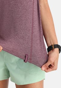 Maglietta sportiva color marrone scuro realizzata in tessuto testurizzato, con etichetta sull'orlo. Abbinata a pantaloni corti verde chiaro, con una vestibilità rilassata e un design casual.