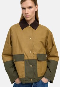 Brązowa i zielona kurtka z blokami kolorów, wykonana z teksturowanej tkaniny, z kołnierzem z sztruksu i zapięciem na napy, z przednimi kieszeniami.