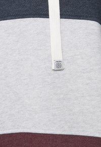 Kapuzenpullover mit grauen, marineblauen und burgunderroten horizontalen Streifen, aus weichem Baumwollstoff mit einem weißen Zugband und einem Etikett.