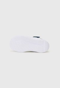 Semelle de sneaker blanche avec un motif de traction texturé ; présente un dessus en tissu bleu marine et un accent vert sur l'onglet du talon.